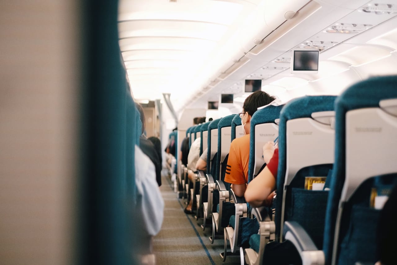Passengers seated in rows of teal seats along the aisle of an airplane cabin