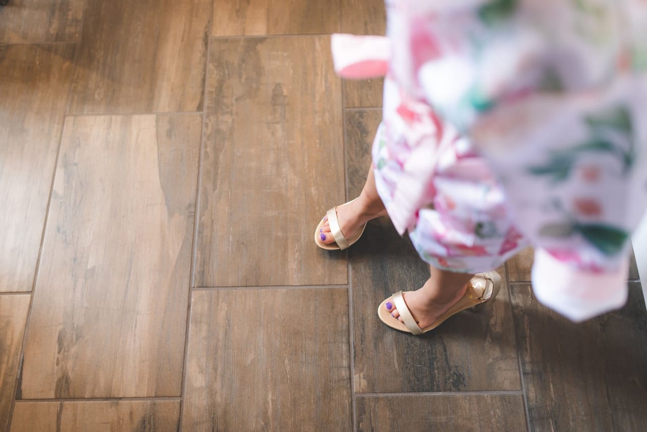 Feet in pale ankle-strap sandals taking a step on a hard wood-look floor