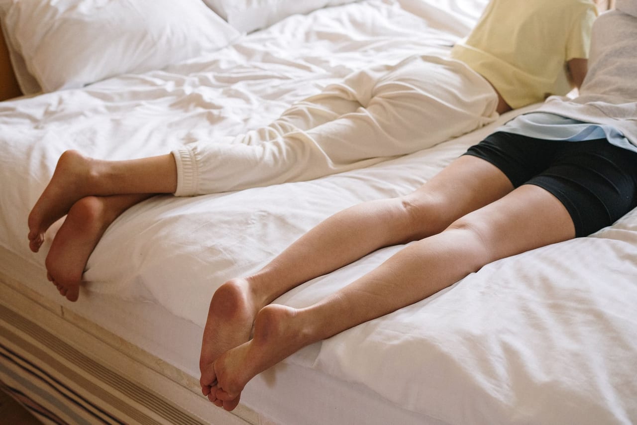 Two people lying on a white bed with bare feet resting at the edge