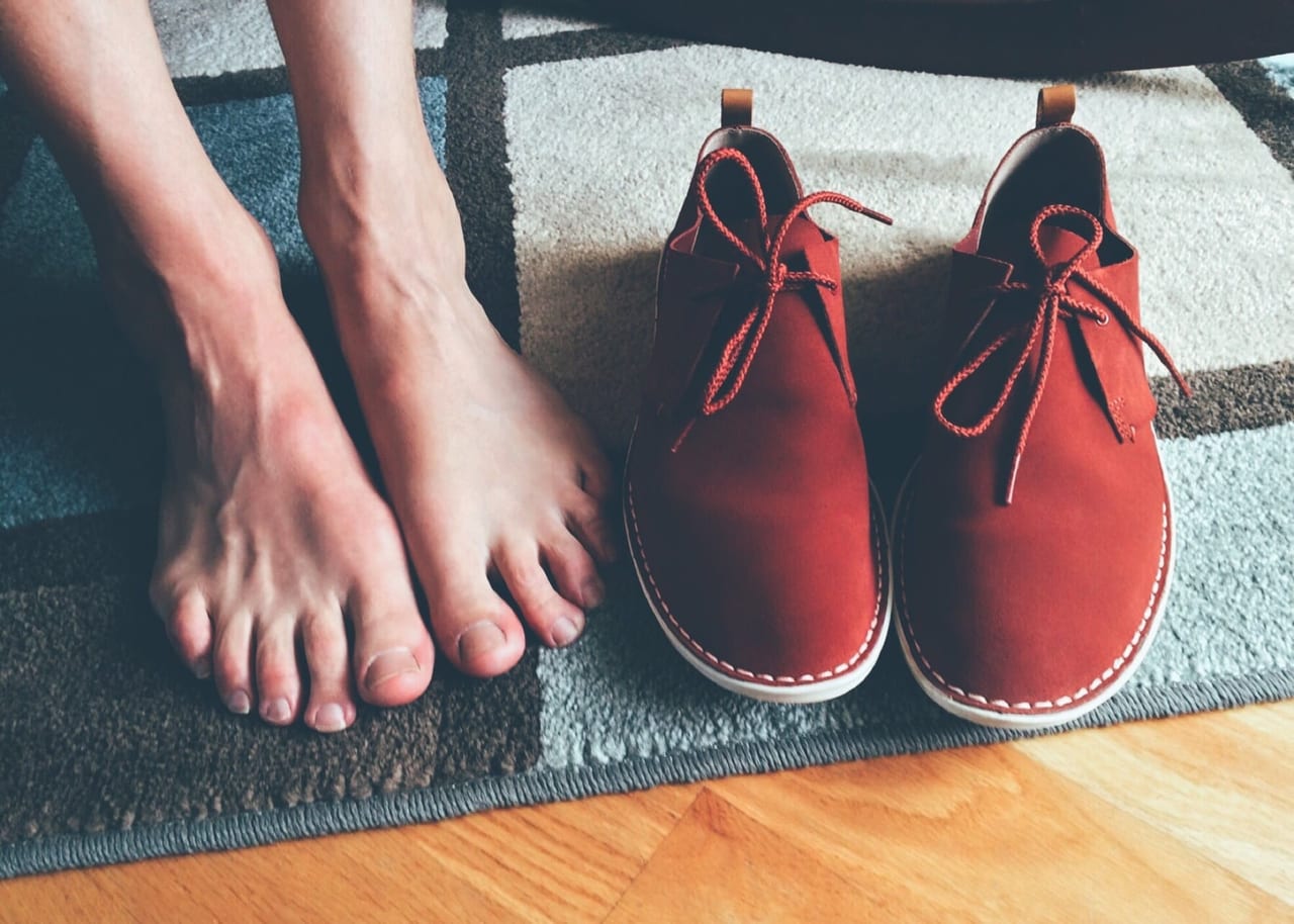 Bare feet on a patterned rug beside a pair of red suede lace-up shoes