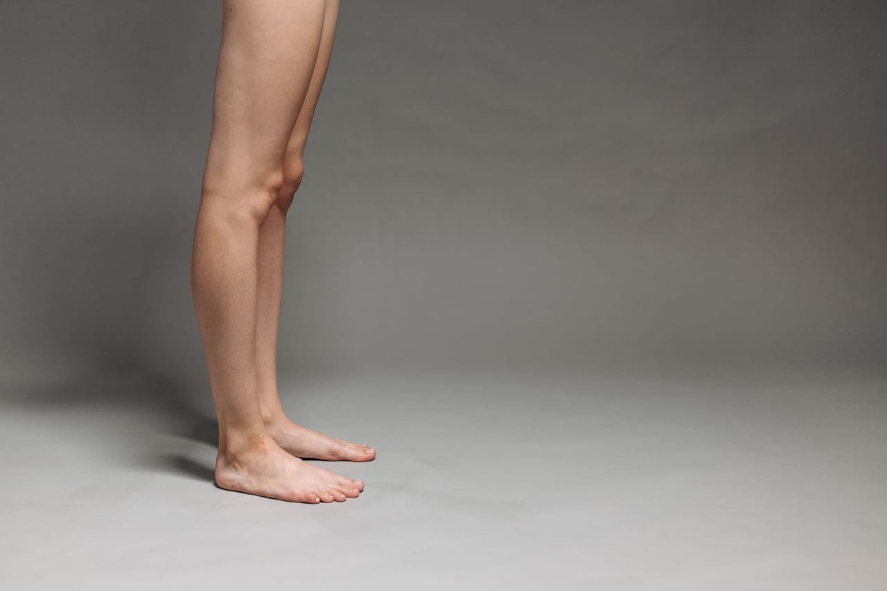 Bare legs and feet standing side by side on a plain grey studio floor