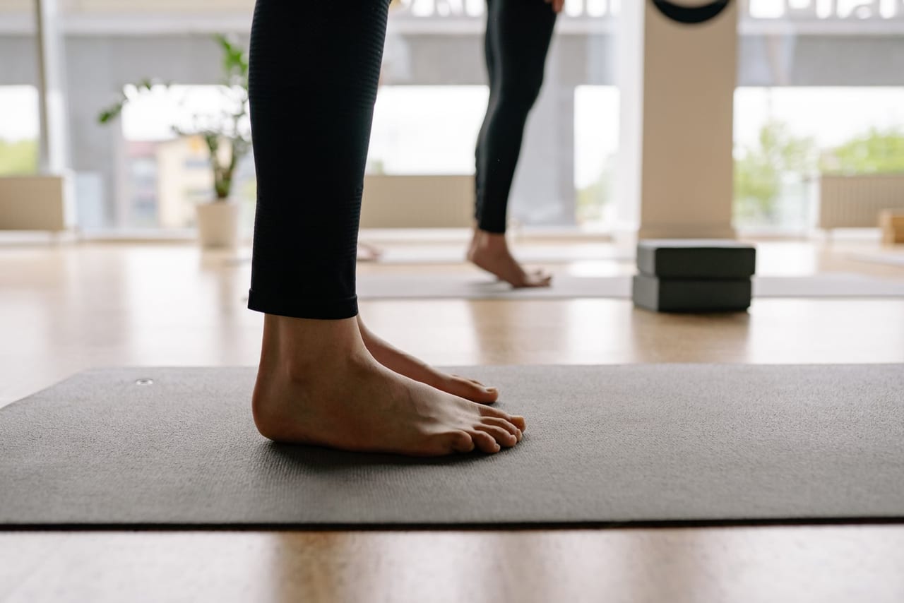 Bare feet standing flat on a gray yoga mat in a bright studio