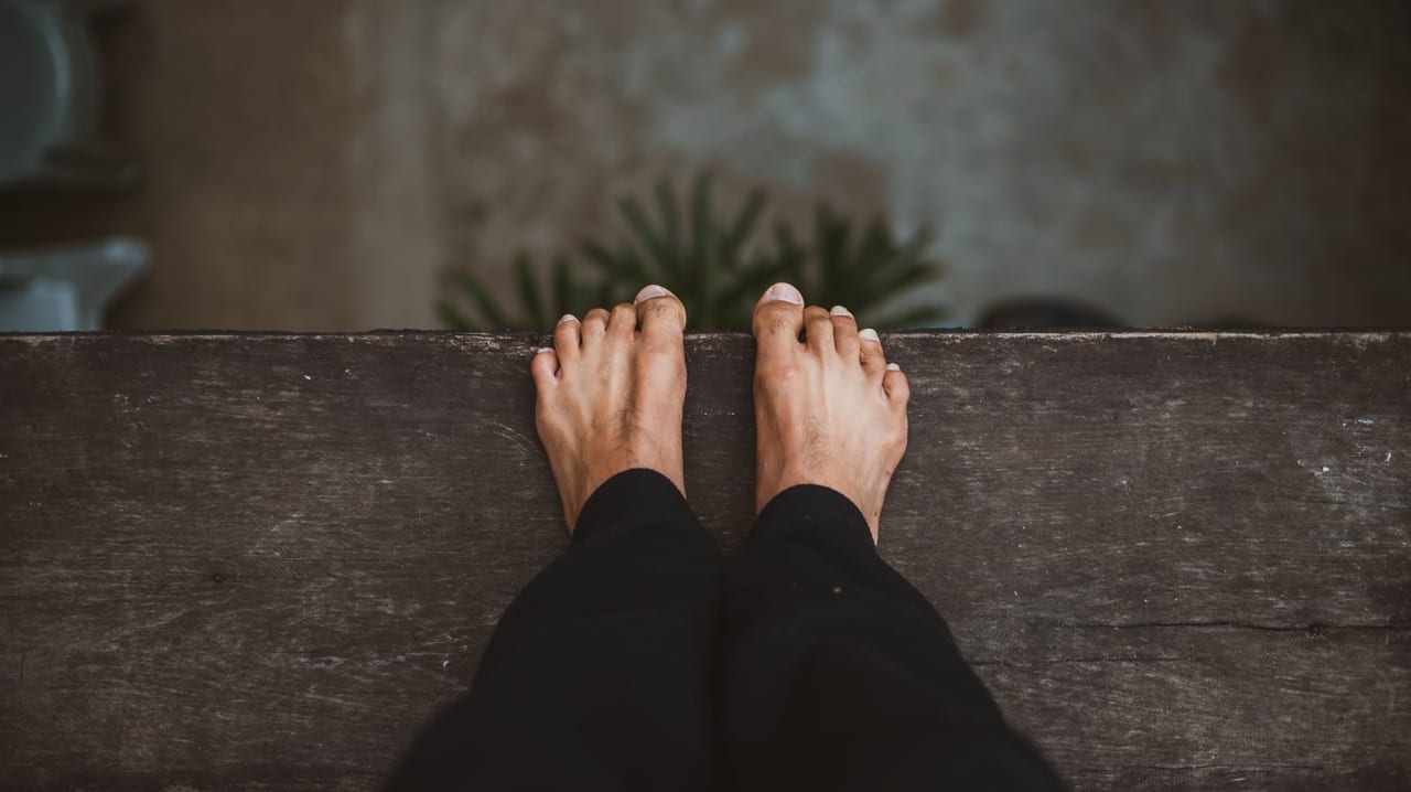 Bare feet seen from above, toes curled over the edge of a dark wooden step