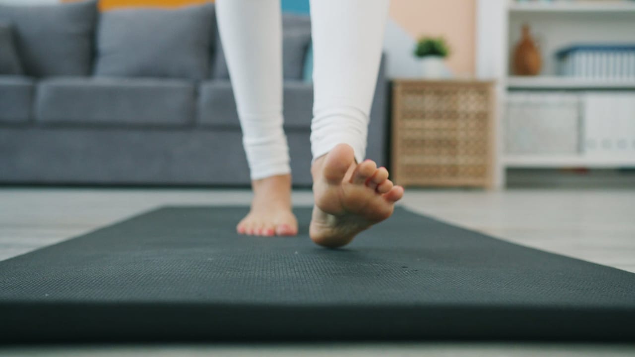 Bare feet and white leggings stepping along a dark exercise mat in a living room