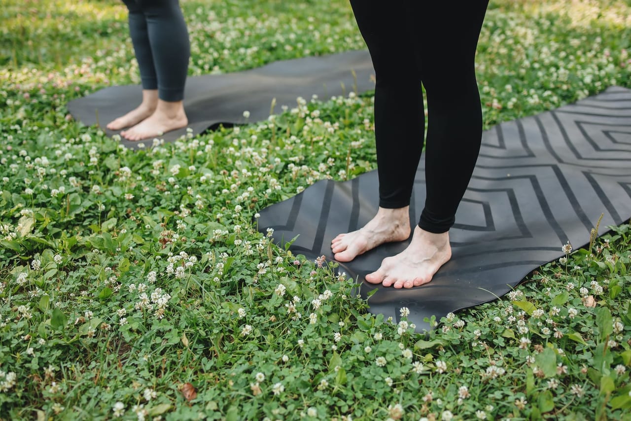 Two people standing barefoot on yoga mats laid out on a clover-dotted lawn