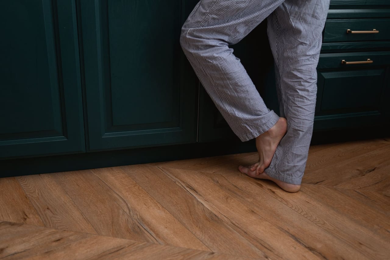 Person in striped pajama trousers standing barefoot on a wooden floor by dark green cabinets