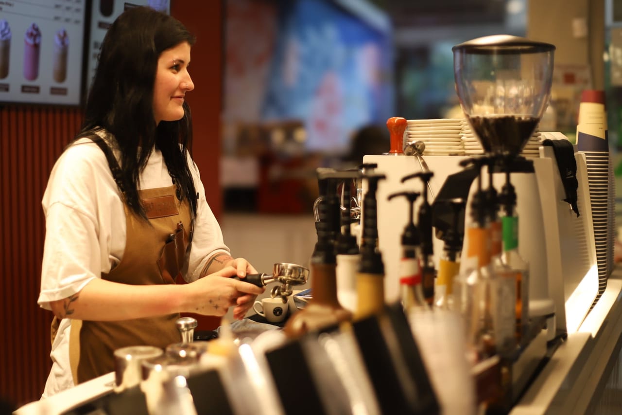 Barista in a brown apron working at an espresso machine behind a cafe counter