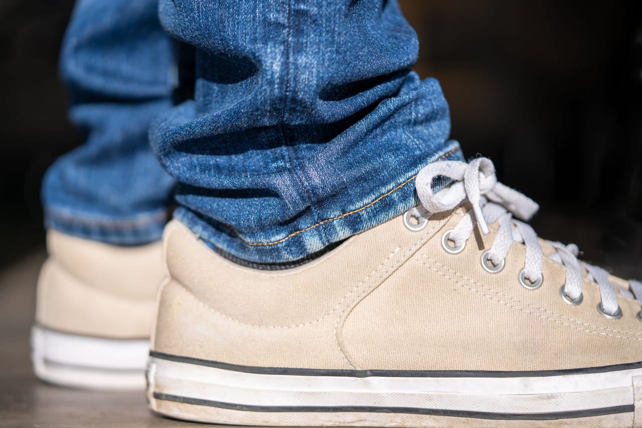 Close-up of beige canvas sneakers with white rubber soles under rolled blue jeans