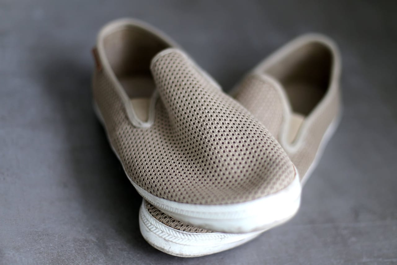 Pair of beige mesh slip-on shoes with white soles on a gray floor