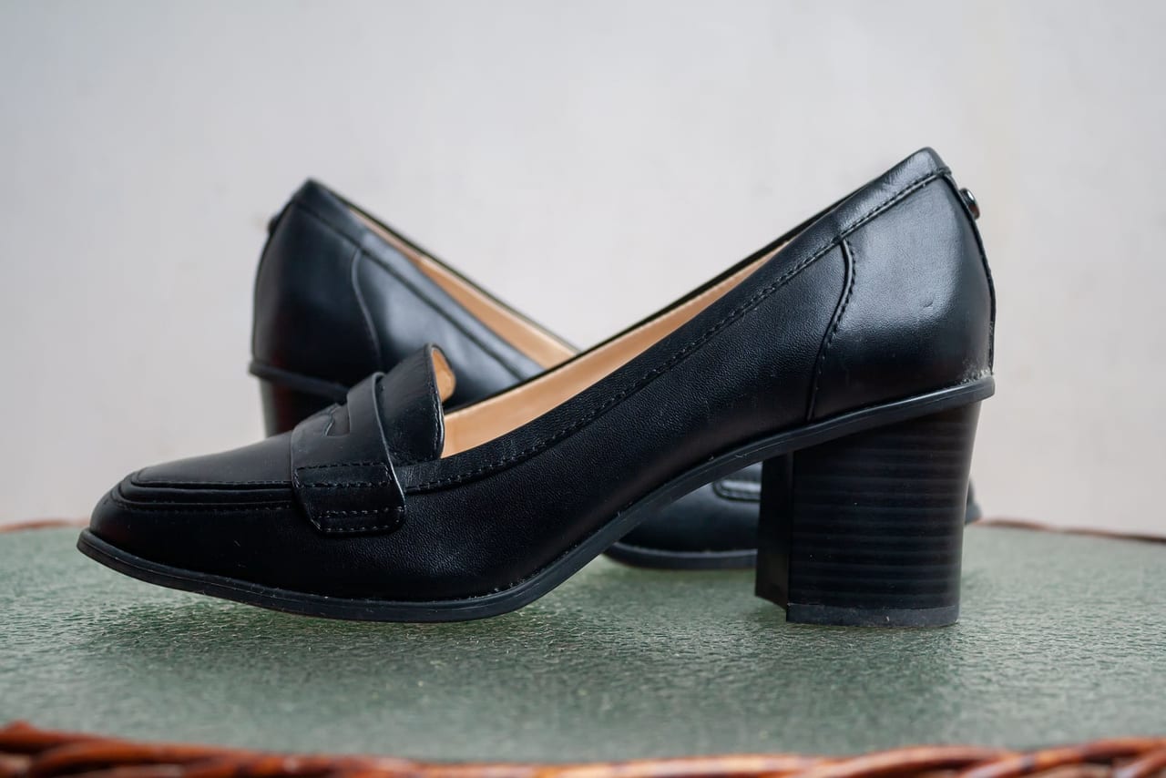 A pair of black leather loafers with wide block heels on a green glass table