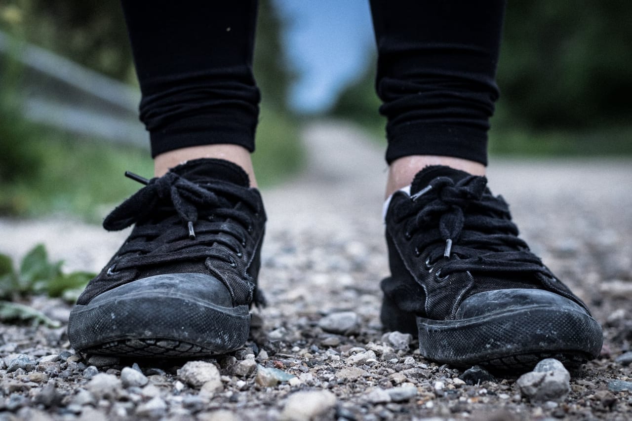 Black lace-up sneakers and ankles of a person standing on a gravel path