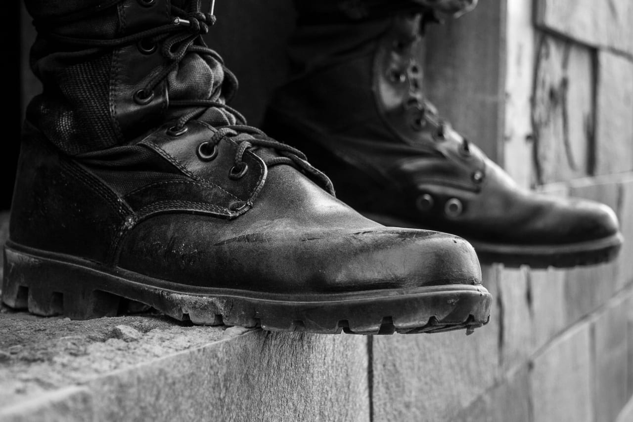Black-and-white close-up of scuffed leather work boots with lug soles on a stone ledge