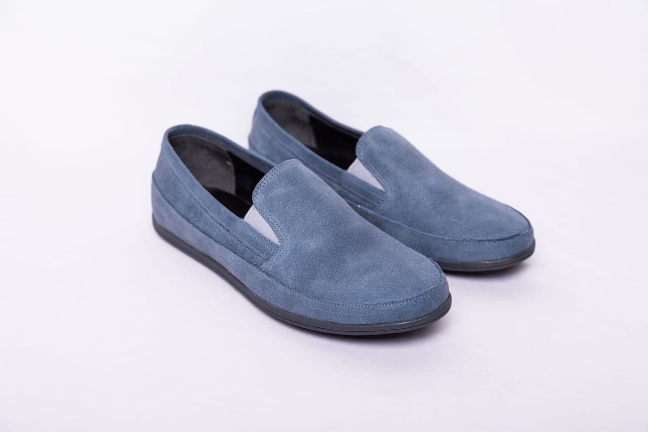 Pair of blue suede slip-on shoes on a plain white background