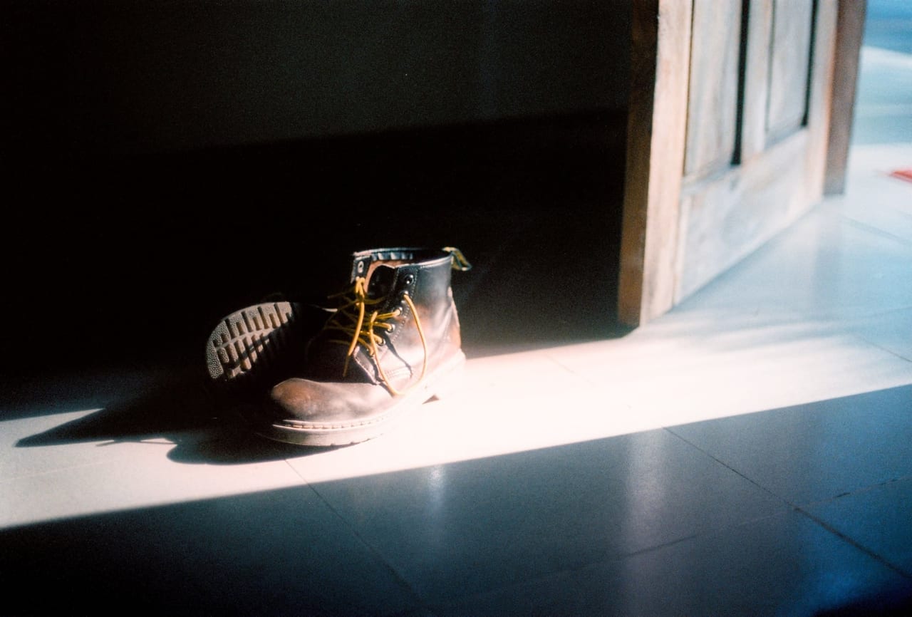 Pair of worn leather boots with loosened yellow laces in sunlight by an open door
