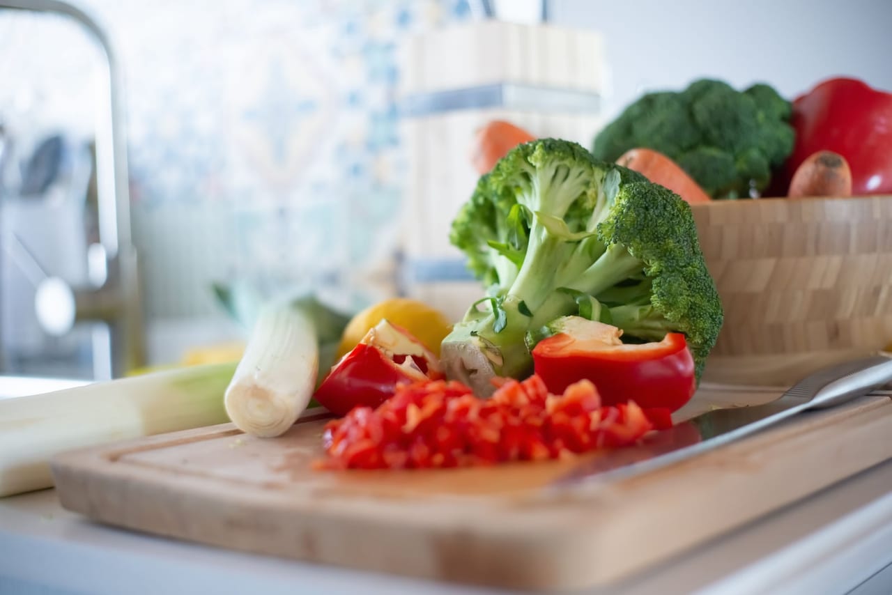 Broccoli and chopped red pepper on a wooden cutting board on a kitchen counter
