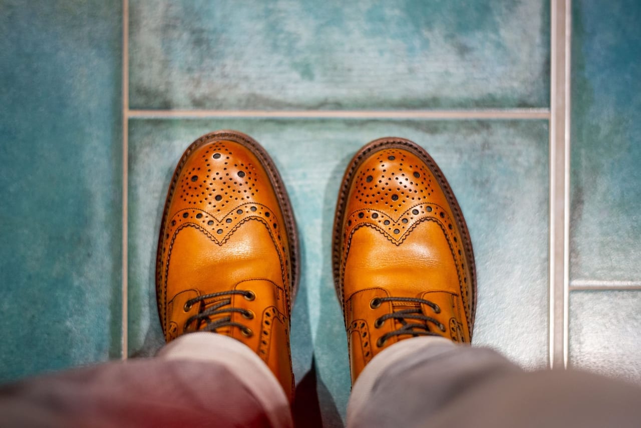 Pair of brown leather brogues with rounded toes seen from above on blue floor tiles