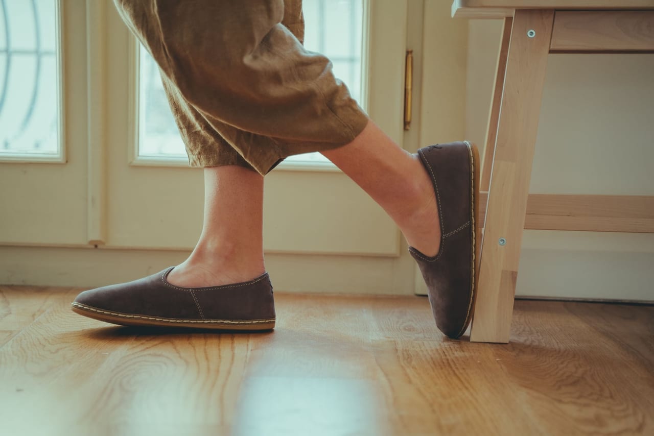 Brown slip-on shoes and loose pants on a wooden floor beside a glass-paned door