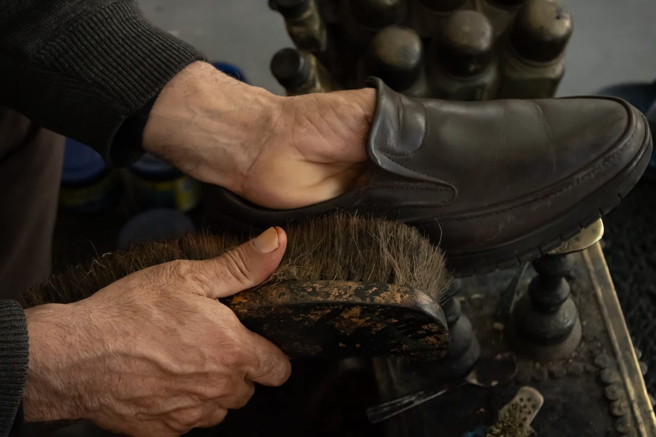 Hands brushing a dark brown leather shoe with a wooden bristle brush