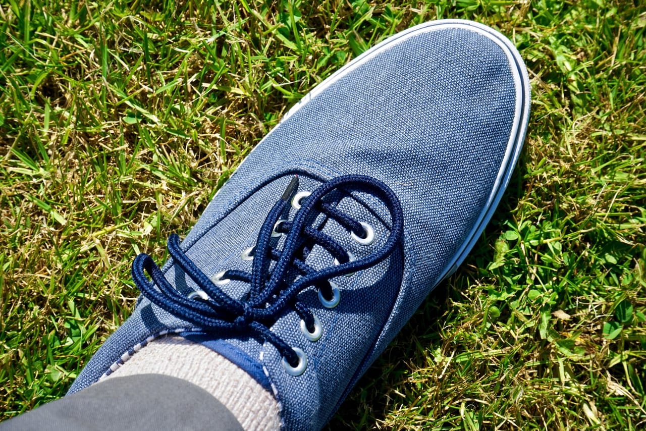 Blue canvas lace-up sneaker worn with a gray sock on a sunny patch of grass
