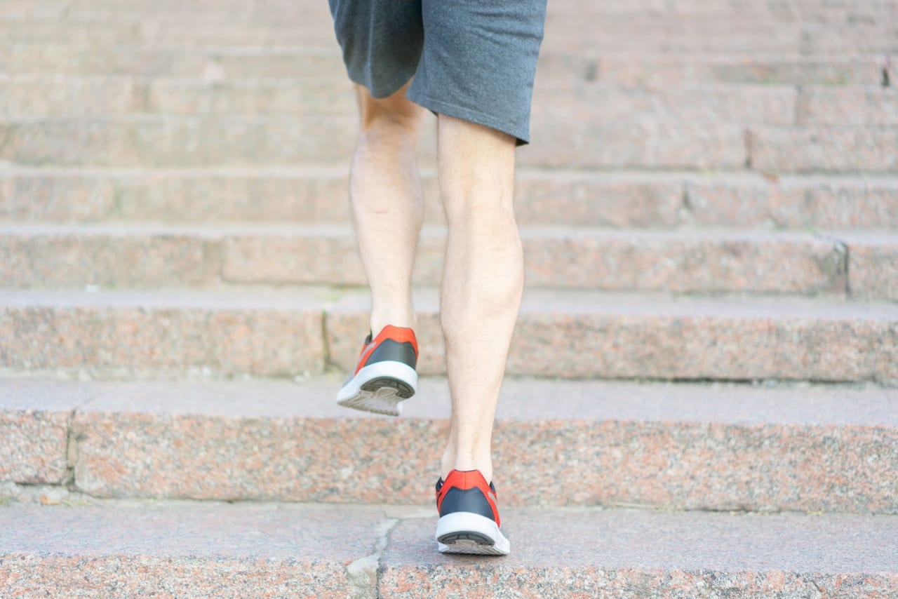 Back view of a person in shorts and sneakers climbing stone steps, one heel lifted