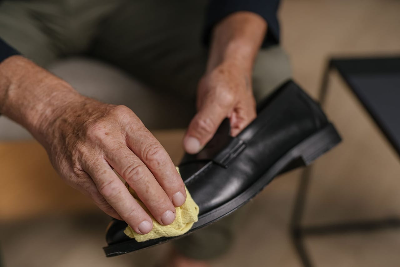 Hands rubbing the toe of a black leather loafer with a small yellow cloth