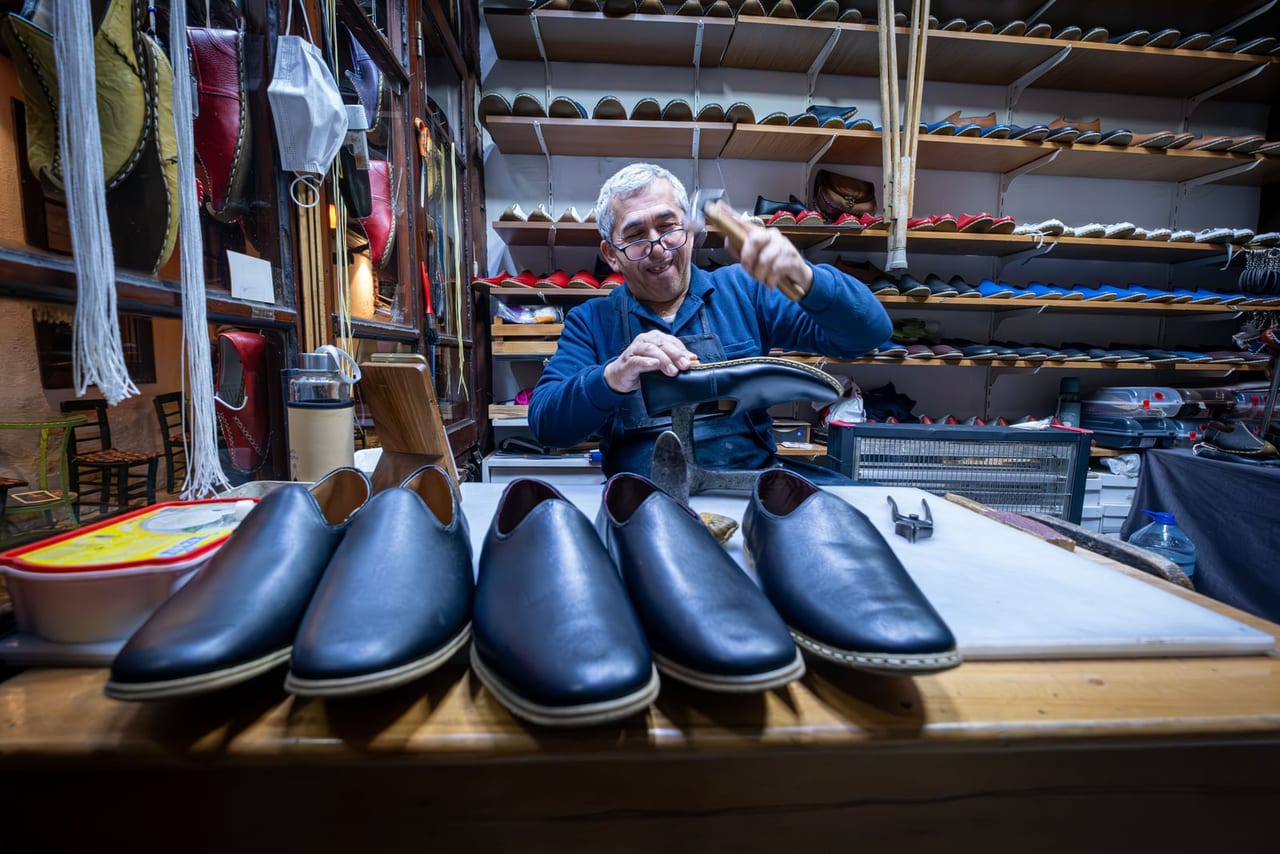 Cobbler hammering a shoe on an iron last in his workshop, black leather slip-ons in front