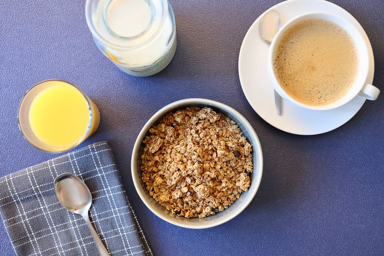 Cup of coffee, glass of juice and jar of milk around a bowl of granola