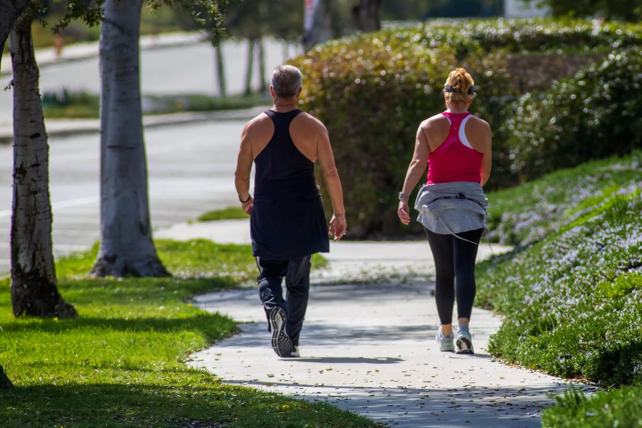 Man and woman in sportswear walking side by side along a smooth, sunlit park path