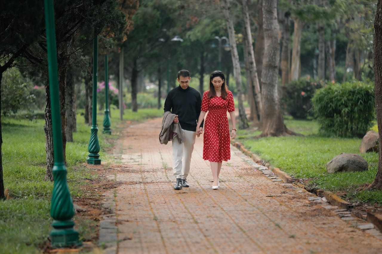 A couple walking hand in hand along a brick path in a tree-lined park