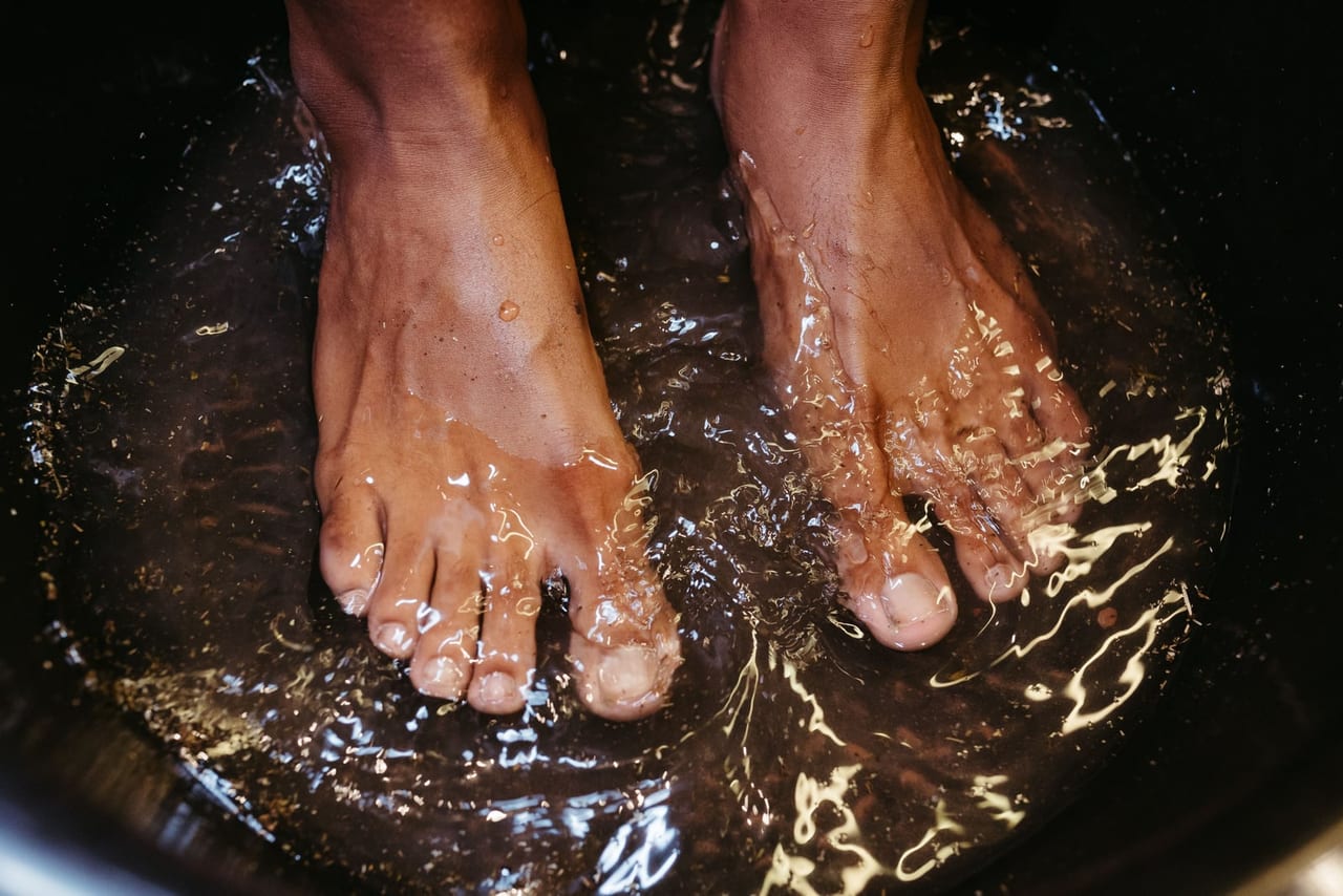 Bare feet in a dark basin of water, with ripples catching the light