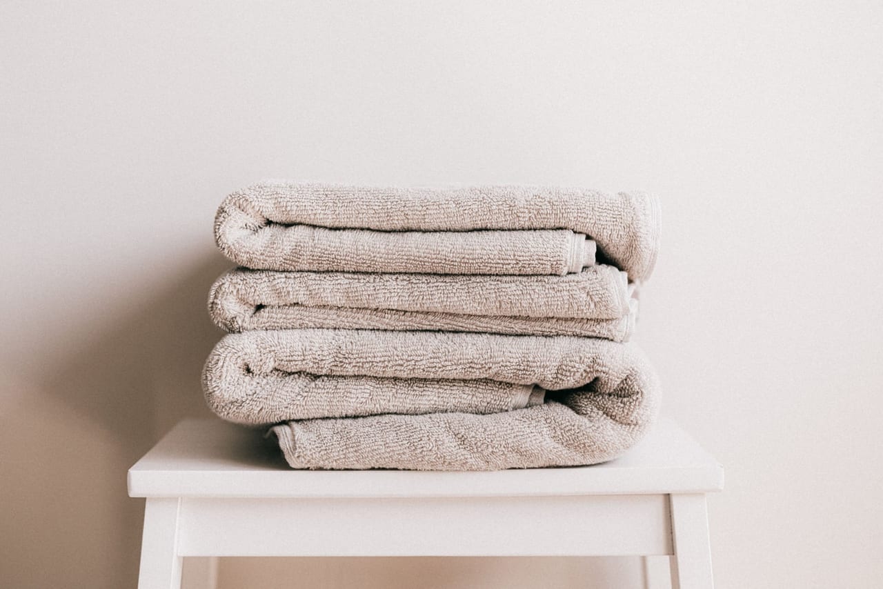 Stack of folded beige towels on a small white stool against a pale wall