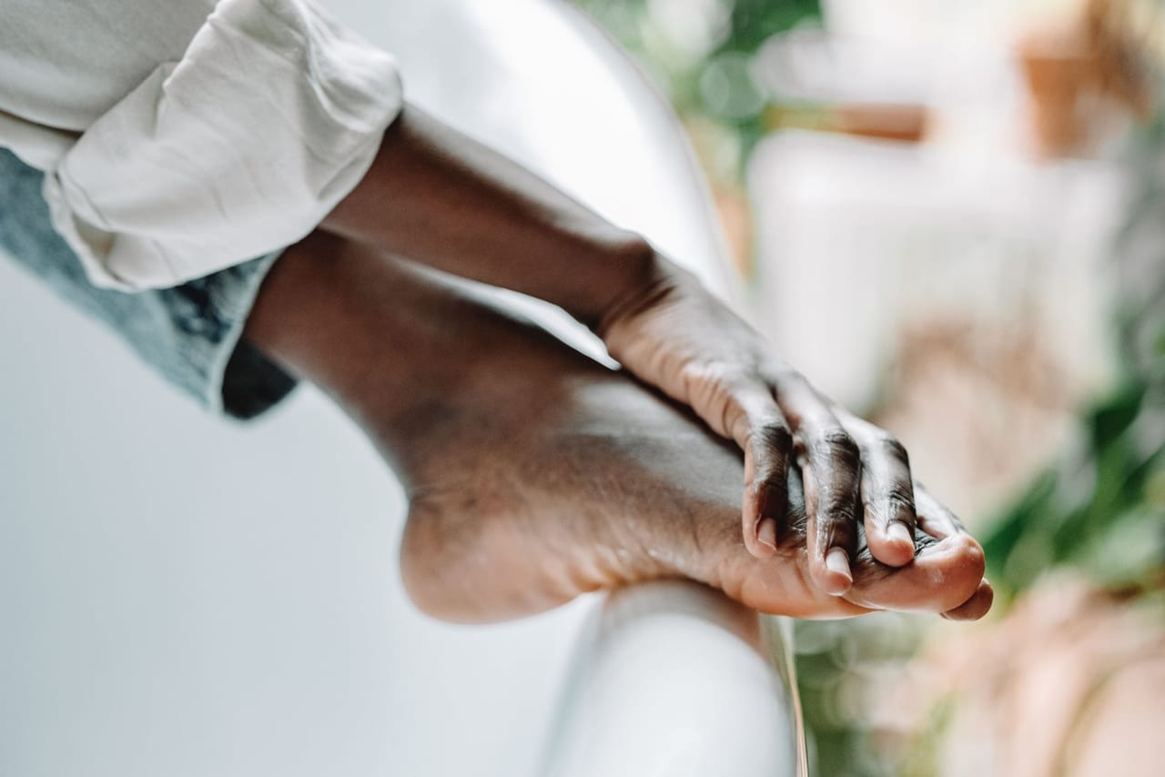 Bare foot resting on the rim of a white bathtub, one hand holding the toes
