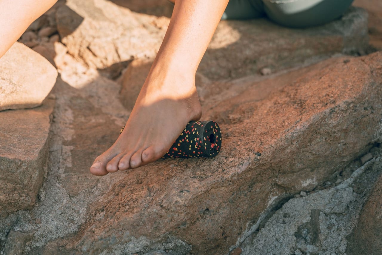 Bare foot rolling a small speckled foam roller across a sunlit rock