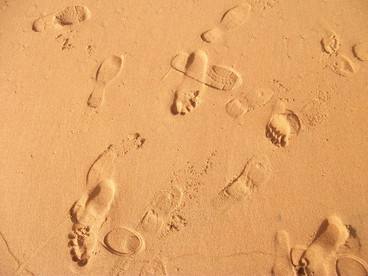 Bare footprints and shoe prints pressed into smooth orange sand
