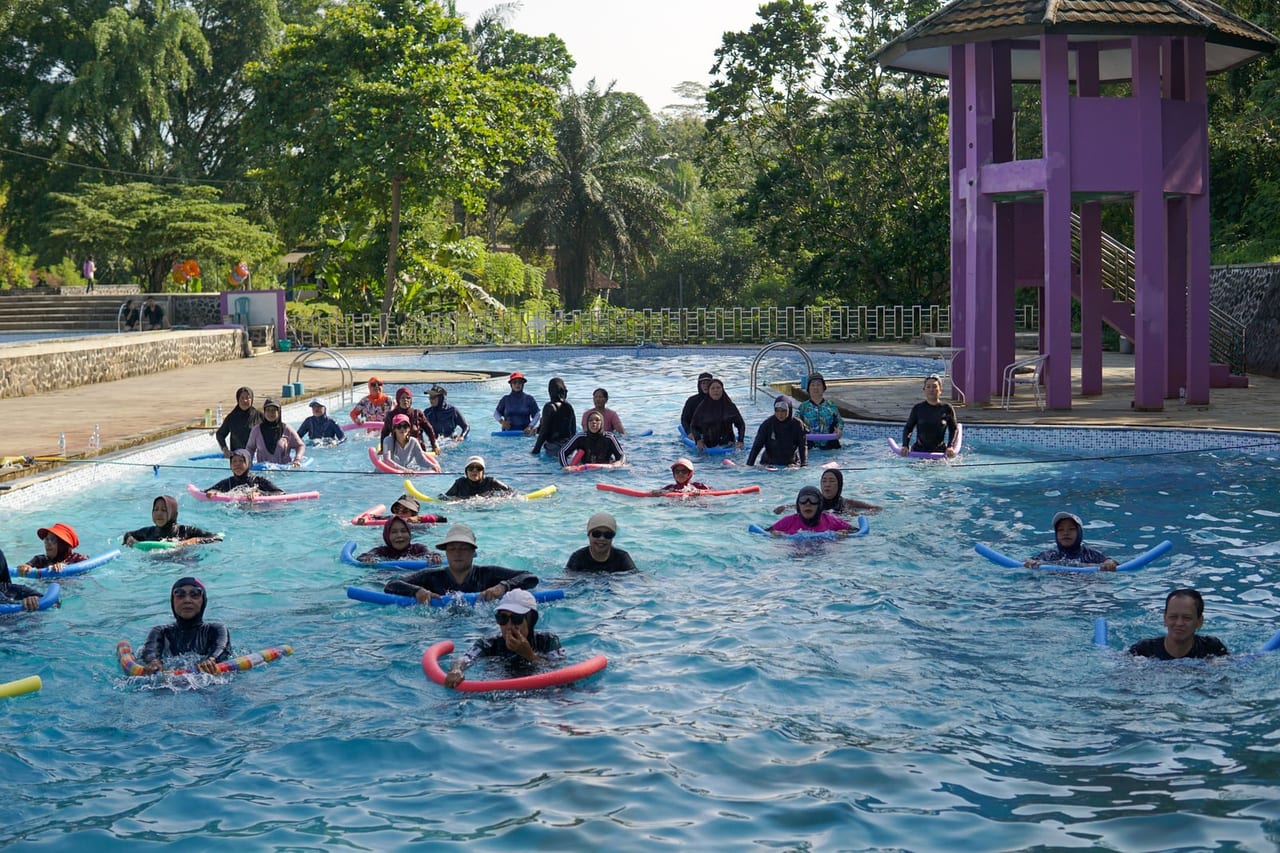 Group of adults standing chest-deep in an outdoor pool, exercising with foam pool noodles