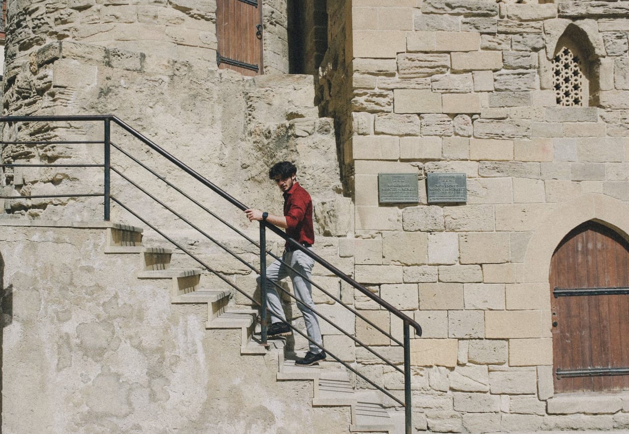 Man in a red shirt walking down worn stone steps, one hand on the metal railing