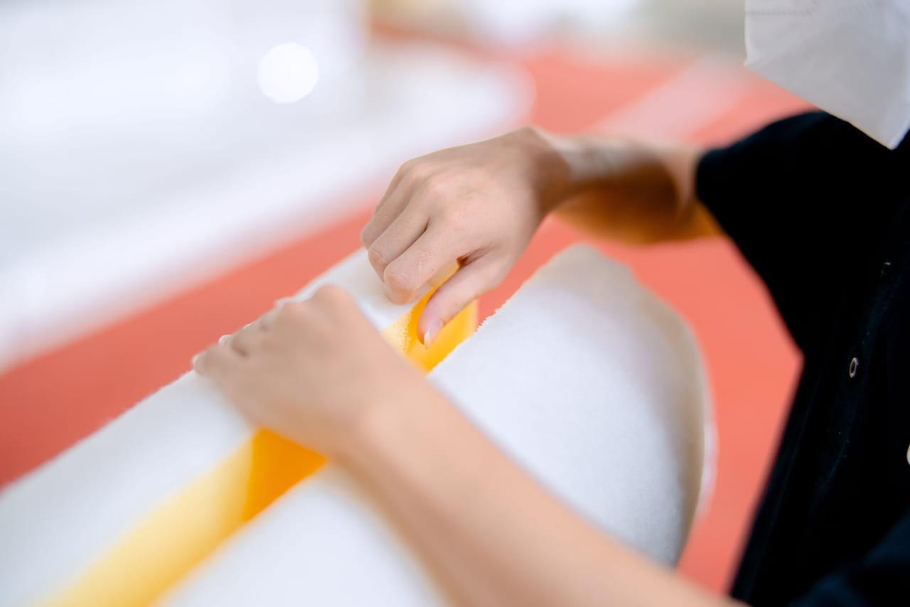 Hands pulling apart layered sheets of white and yellow foam at a workbench