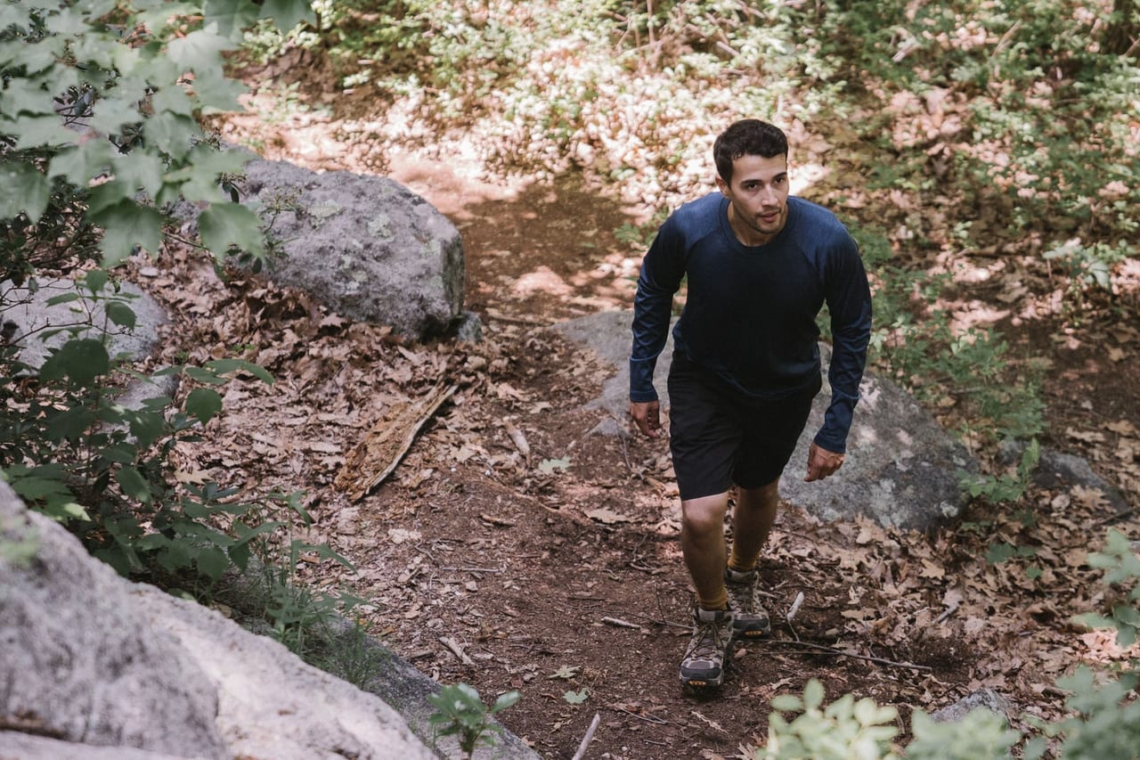 Hiker in a long-sleeved top and shorts walking up a rocky, leaf-covered forest trail