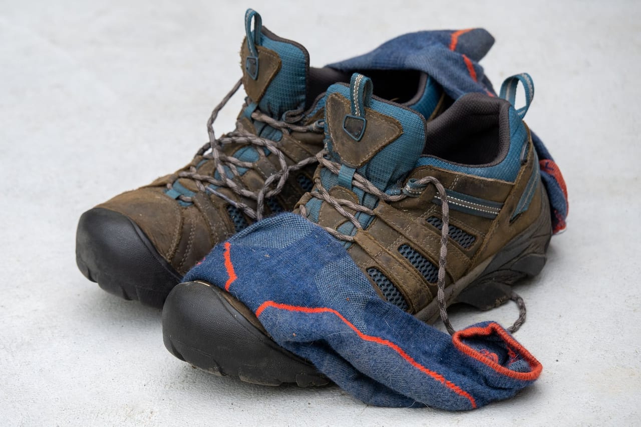 Worn brown hiking shoes with a pair of blue socks draped over them on a pale floor