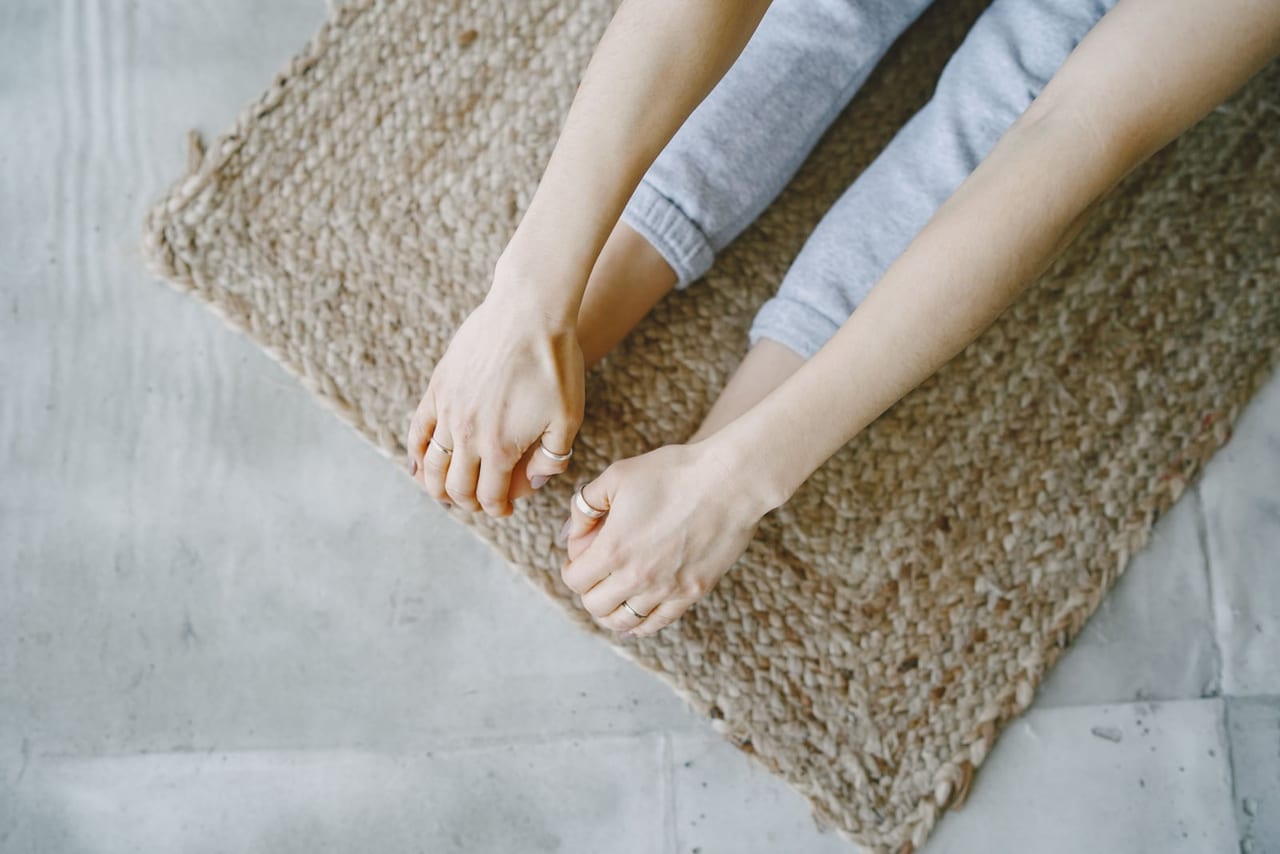 Seated person holding their toes with both hands on a woven jute rug