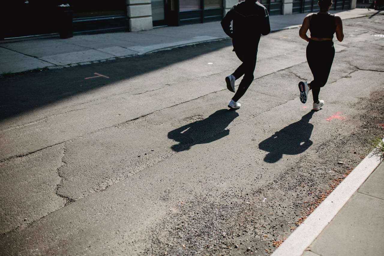 Two joggers in black seen from behind on a cracked, sunlit city street