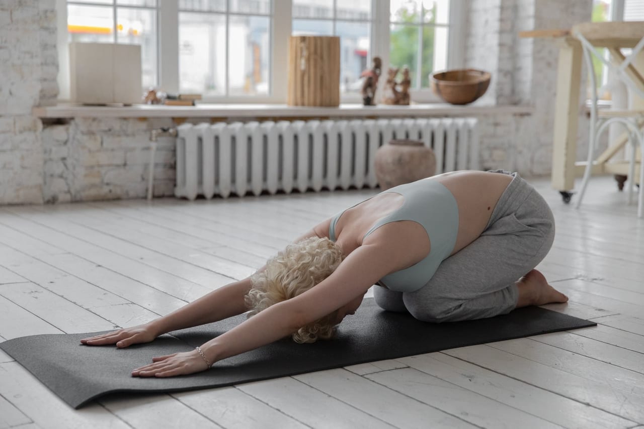 Woman kneeling folded forward on a mat, the tops of both feet flat on the floor