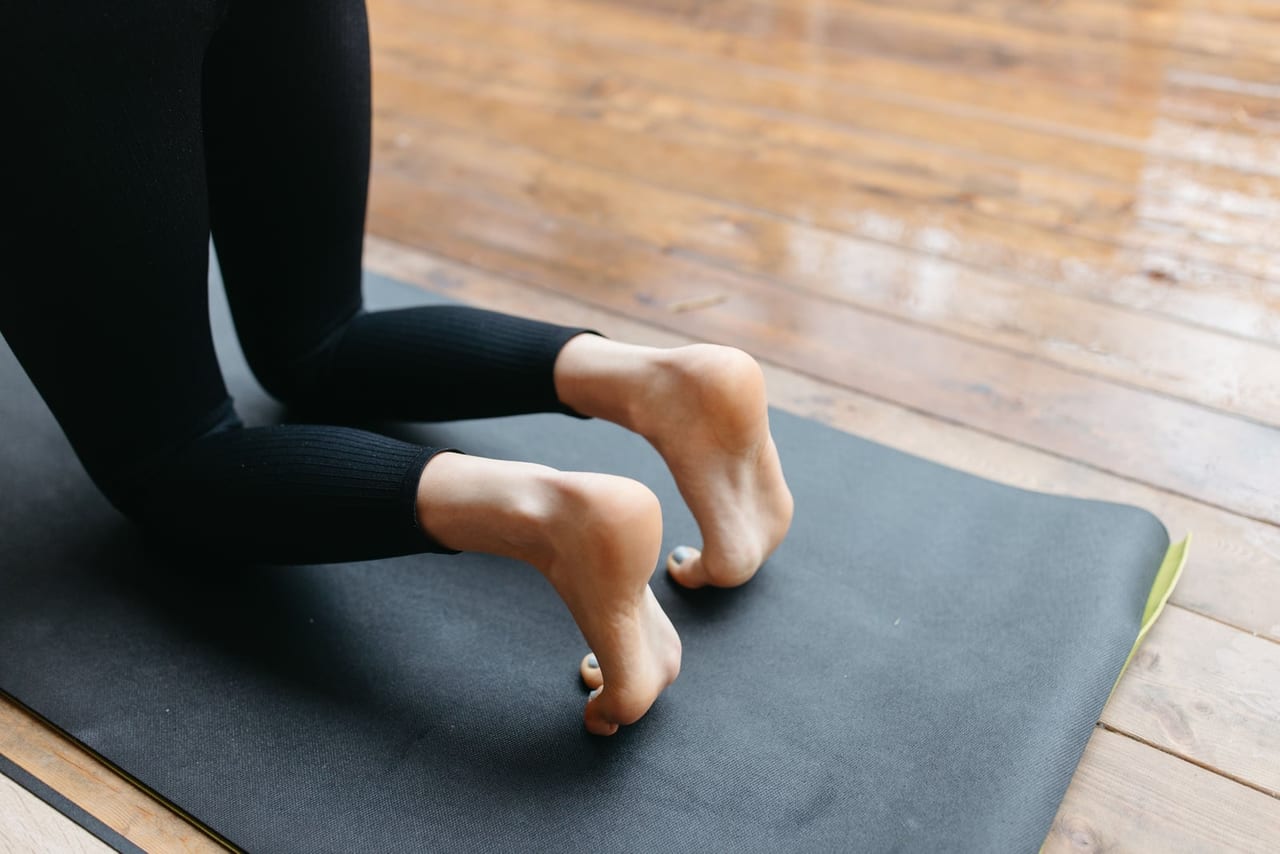 Person kneeling on a black yoga mat with toes tucked under and heels lifted