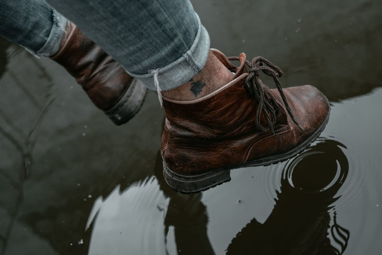 Brown leather lace-up boots stepping into a shallow puddle with ripples around them
