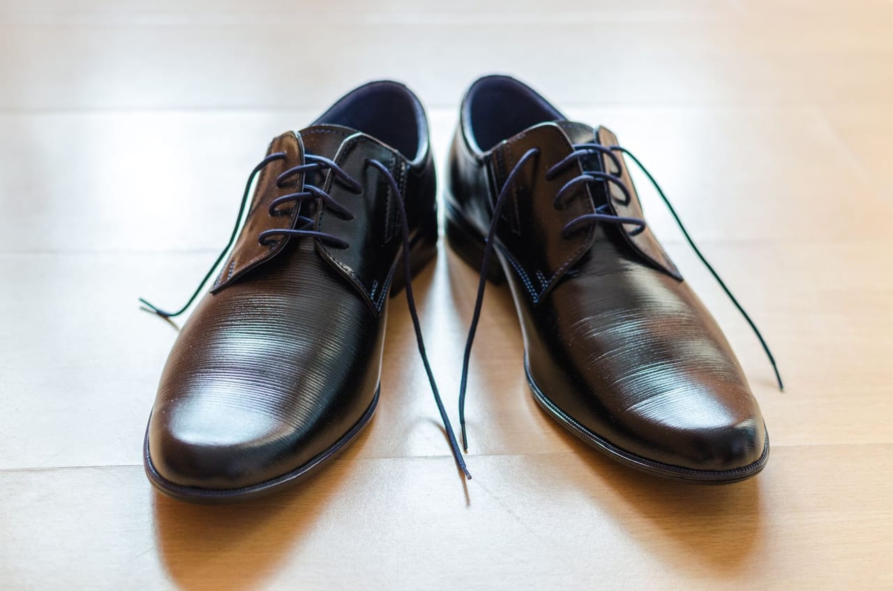 Pair of black leather lace-up shoes with loosened laces resting on a light wooden floor