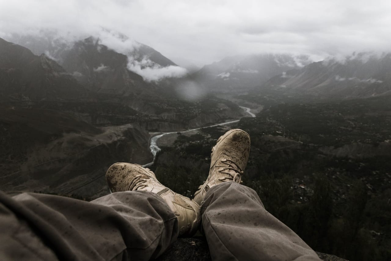A hiker's muddy boots stretched out on a rock above a misty river valley