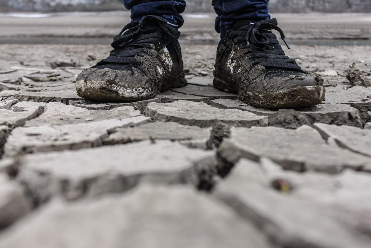 Person standing in mud-caked black sneakers on cracked dry ground
