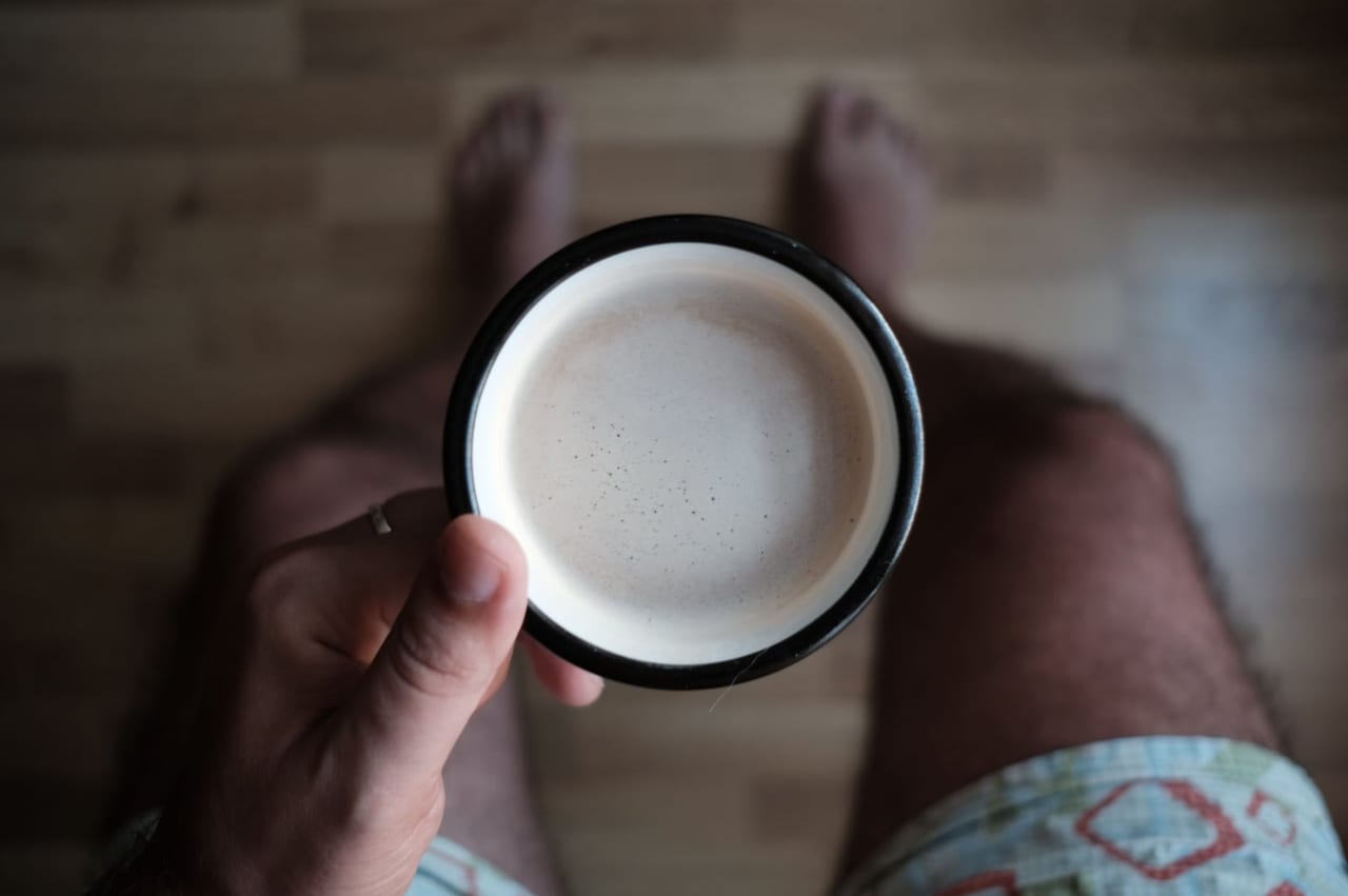 Person holding a mug above bare feet on a wooden floor, seen from above