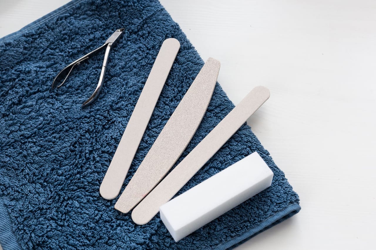 Nail nippers, three emery boards and a white buffer block on a folded blue towel