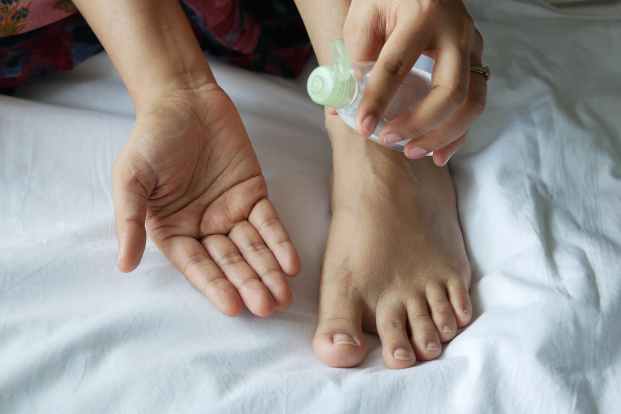 Open palm and a small clear bottle of oil above a bare foot on white sheets
